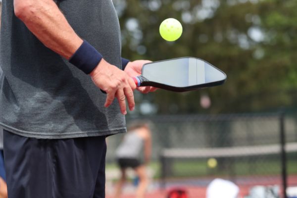 A person holding a pickleball paddle in Needham bounces a yellow pickleball.