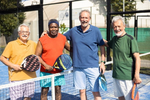 A group of four male seniors happily posing with their tennis racquets at hand.