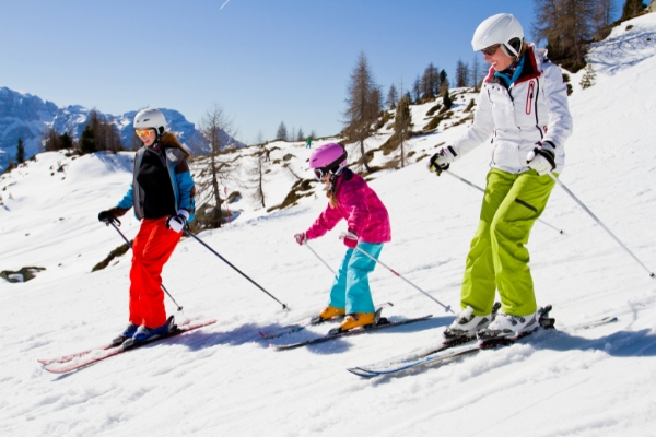 A family skiing on a downward slope in a snowy mountain with their child. Beginner ski gear guide.