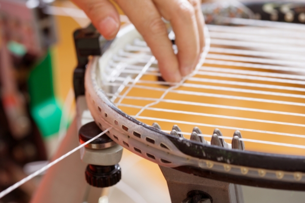 A tennis racquet getting new strings by a professional tennis racquet restringer.