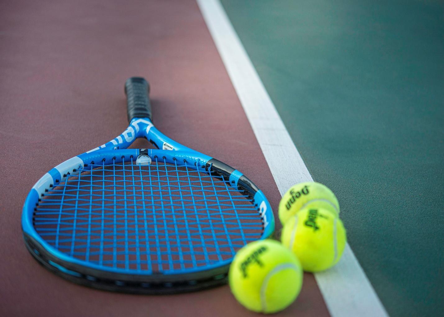 A tennis racquet on a court with three tennis balls.